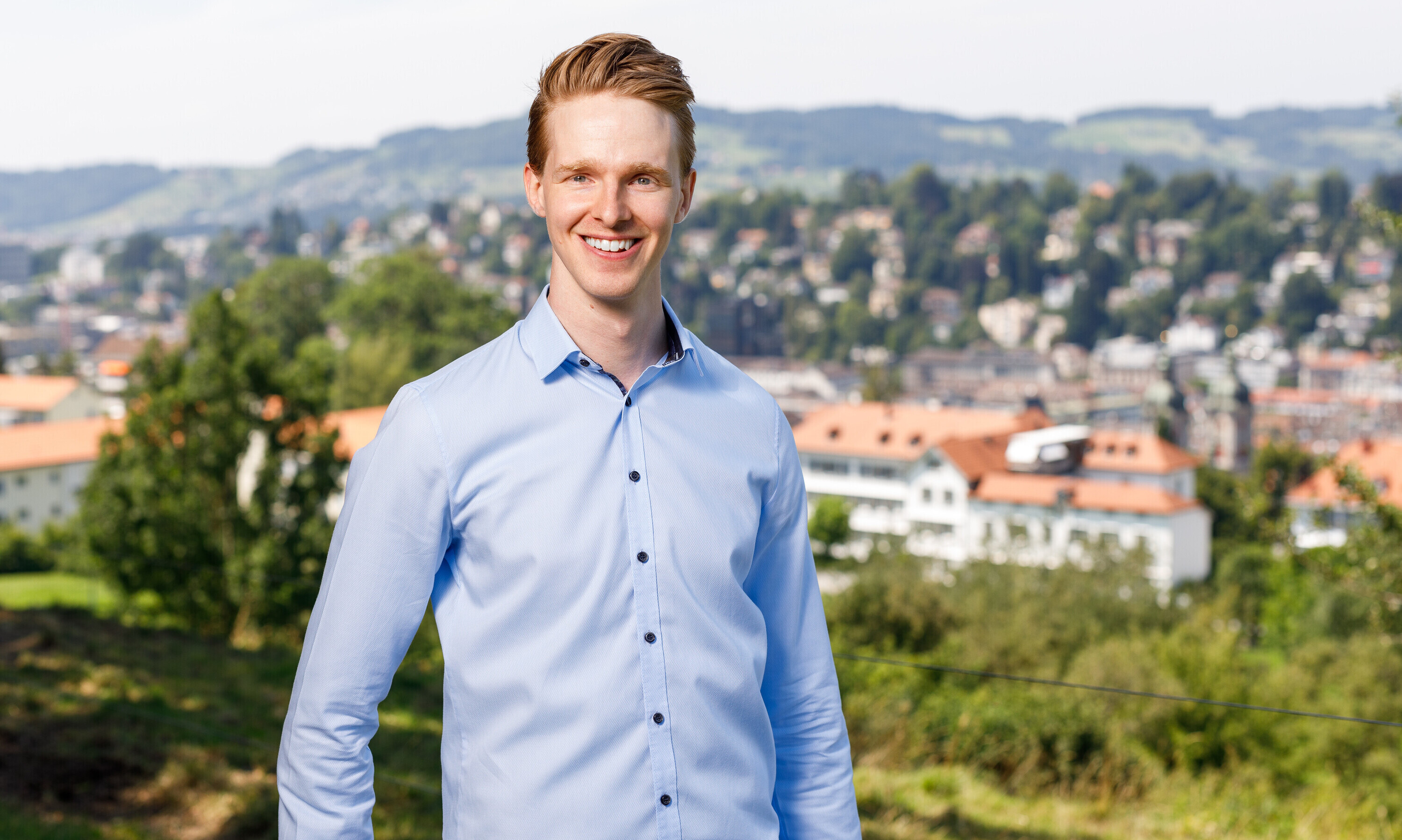 Das Porträt zeigt Lars Bittel in einem hellblauen Hemd; er steht draussen, im Hintergrund ist die Stadt zu sehen.