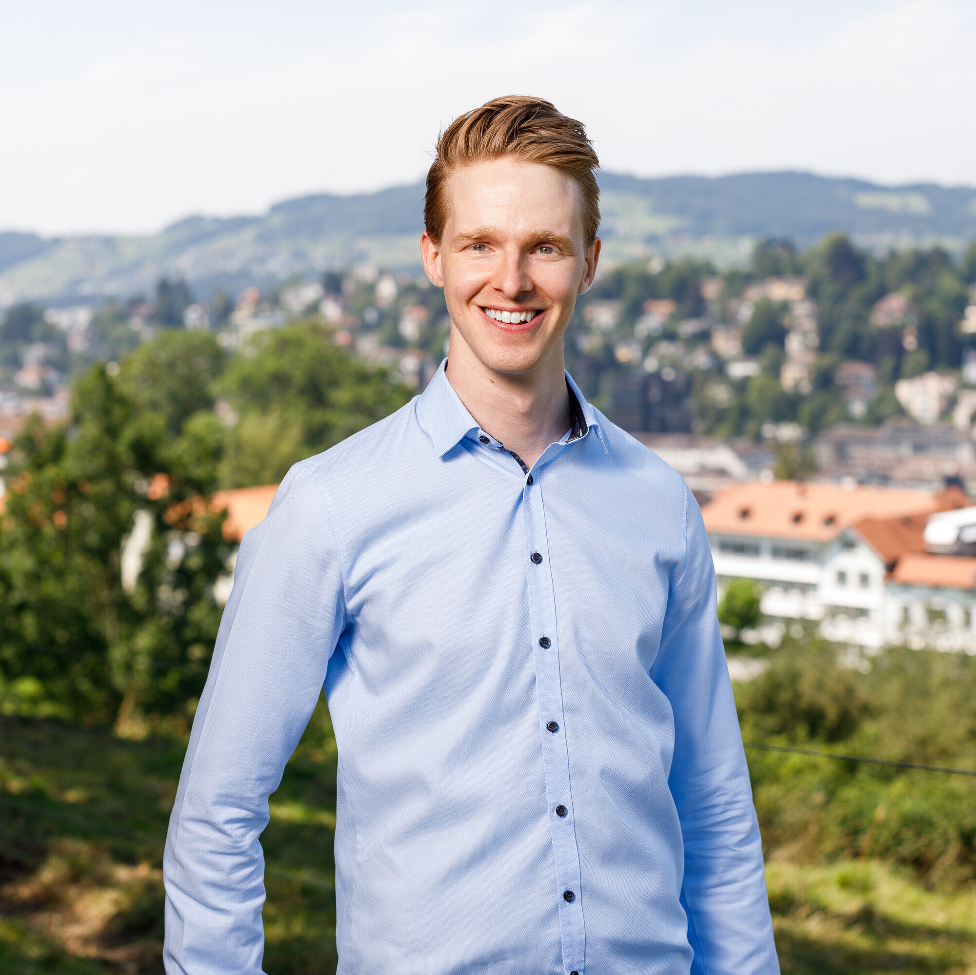 Das Porträt zeigt Lars Bittel in einem hellblauen Hemd; er steht draussen, im Hintergrund ist die Stadt zu sehen.