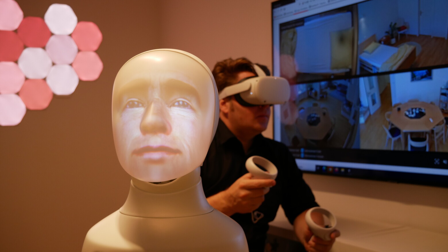 Im Vordergrund ist ein Plastikgesicht als virtueller Sprachassistent zu sehen, im Hintergrund ein Forscher mit VR-Brille.
