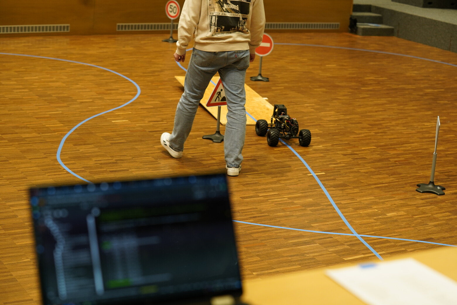 Bei der AI Challenge müssen die Fahrzeuge autonom einer blauen Linie auf dem braunen Hallenboden folgen.