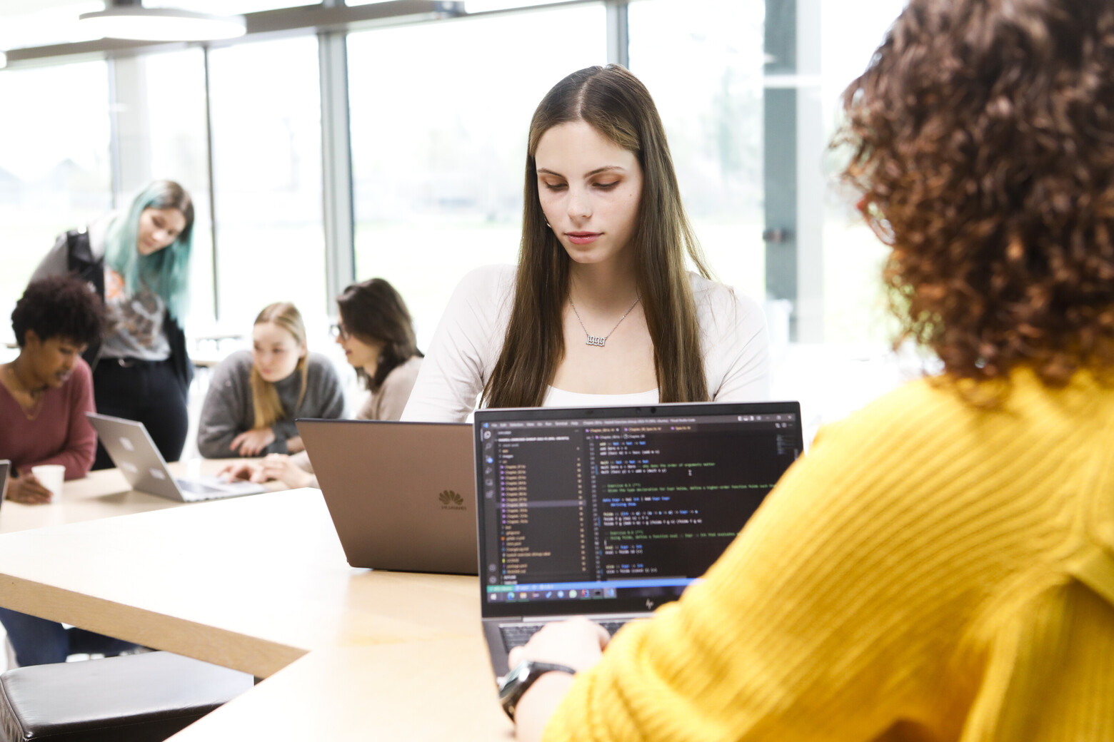 Junge Frauen sitzen an Tischen und programmieren mit Laptops.