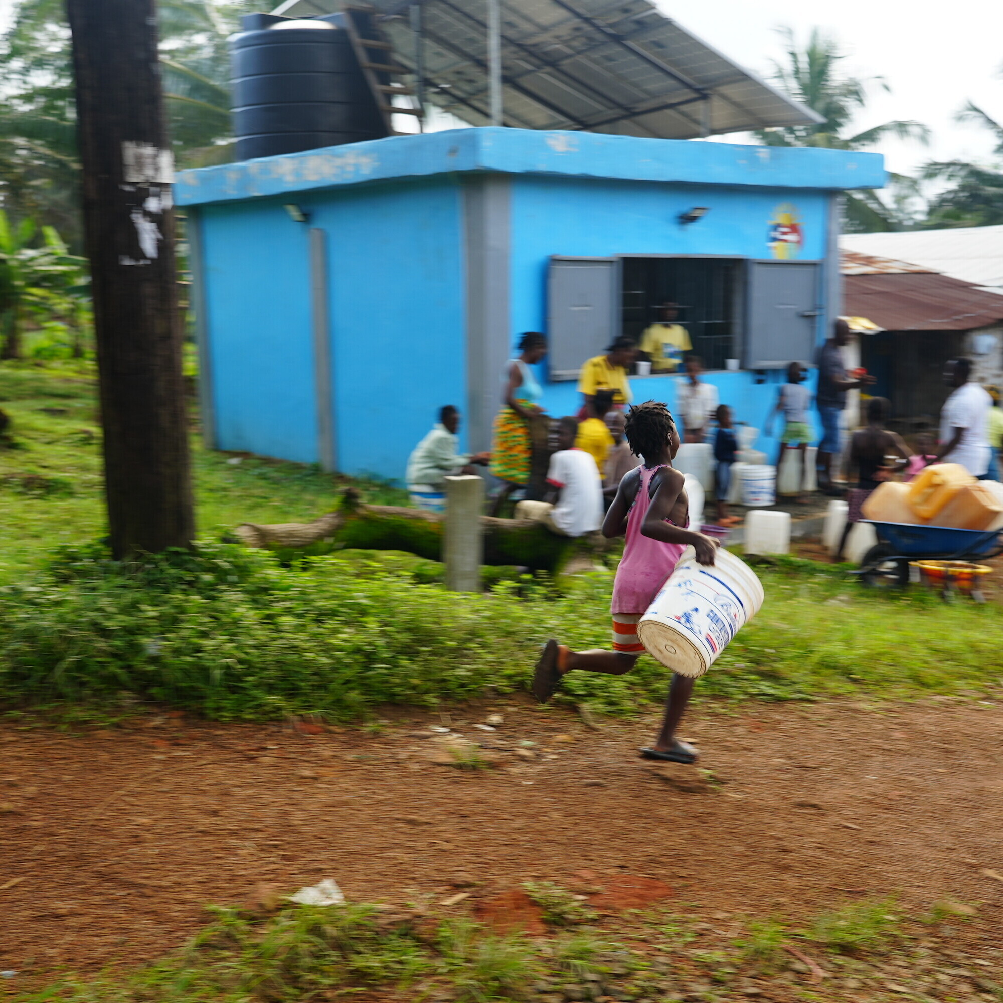 Mit Kübeln ausgerüstet holen Kinder und Erwachsene beim blauen Wasserkiosk sauberes Trinkwasser für ihre Familien.