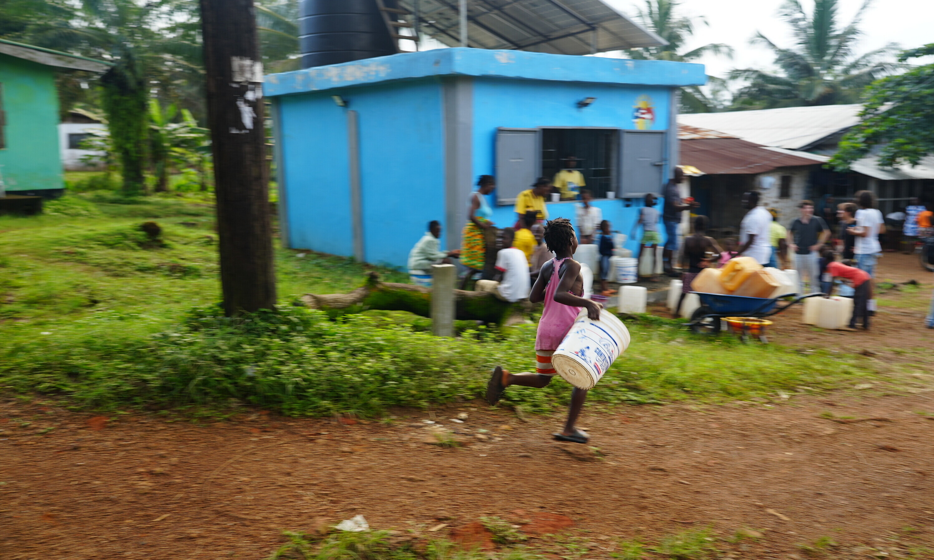 Mit Kübeln ausgerüstet holen Kinder und Erwachsene beim blauen Wasserkiosk sauberes Trinkwasser für ihre Familien.