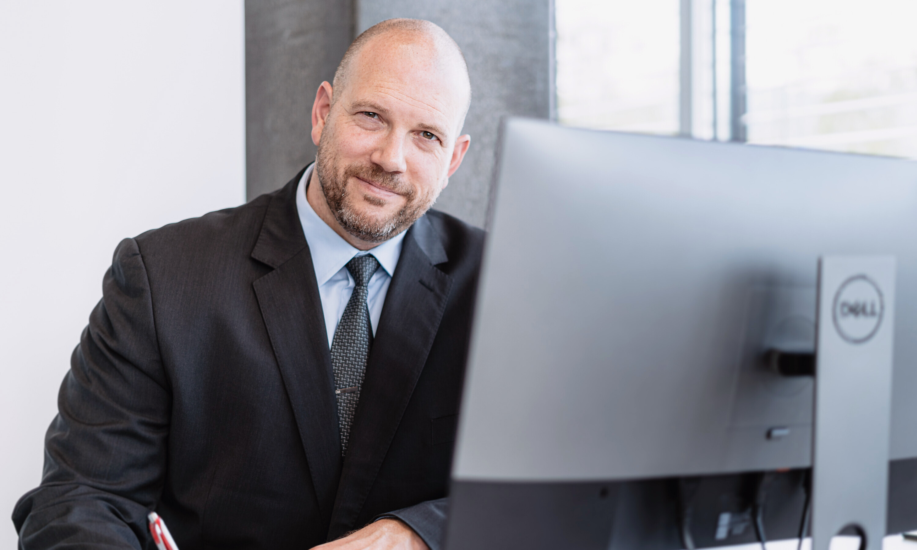 Daniel Seelhofer, Rektor der OST, sitzt hier an seinem Computer, lächelt in die Kamera und hält einen Stift in der Hand.