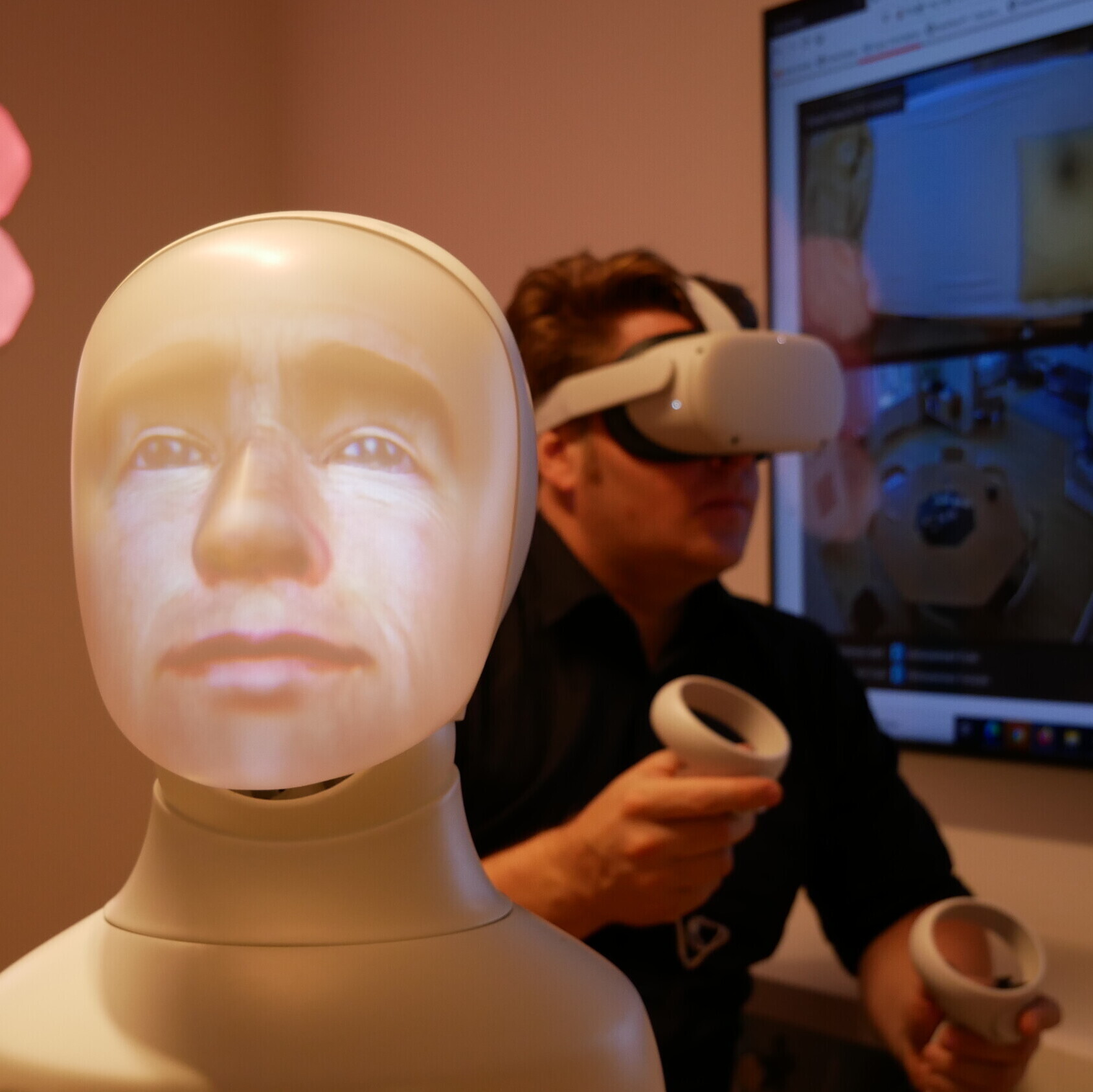 Im Vordergrund ist ein Plastikgesicht als virtueller Sprachassistent zu sehen, im Hintergrund ein Forscher mit VR-Brille.