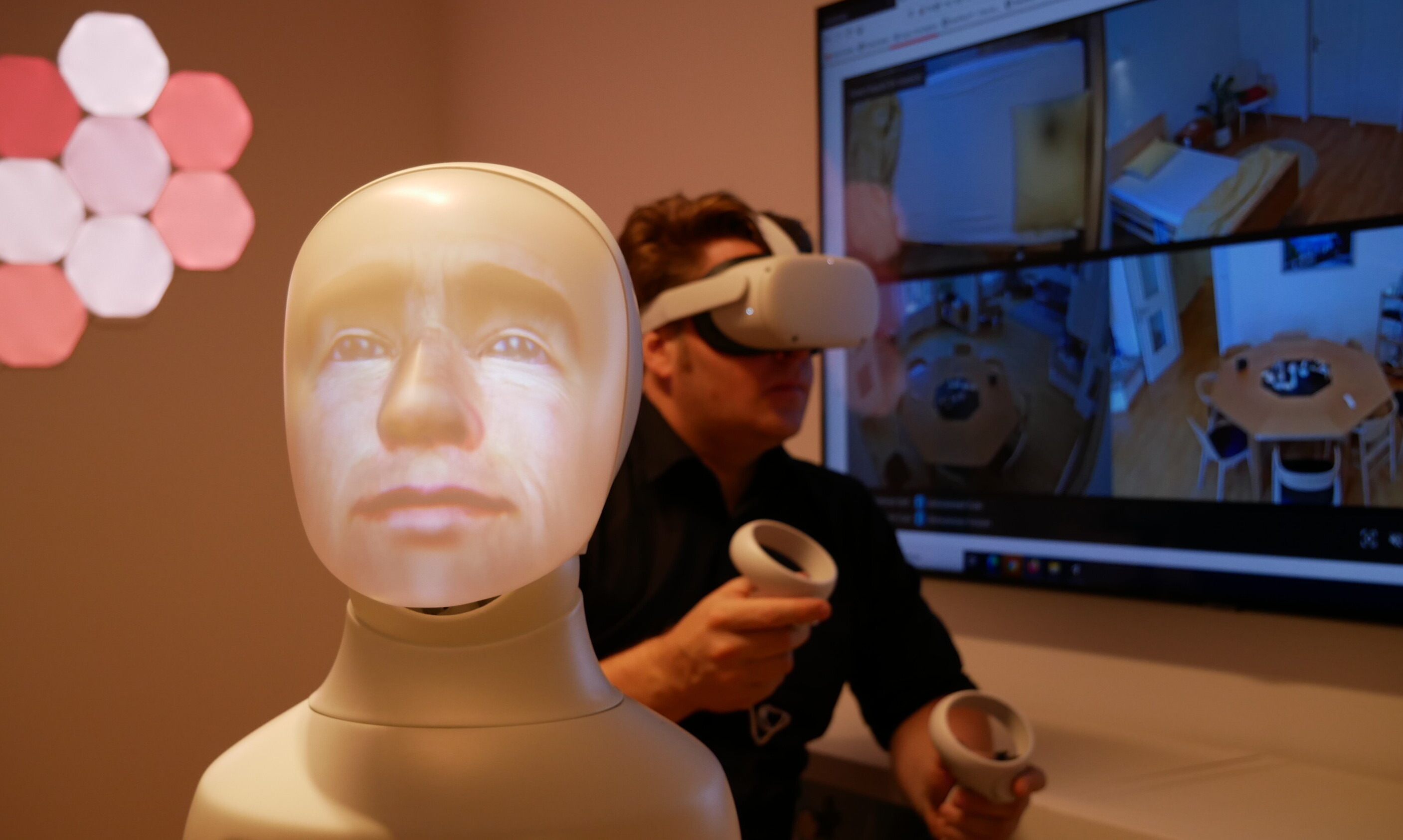 Im Vordergrund ist ein Plastikgesicht als virtueller Sprachassistent zu sehen, im Hintergrund ein Forscher mit VR-Brille.