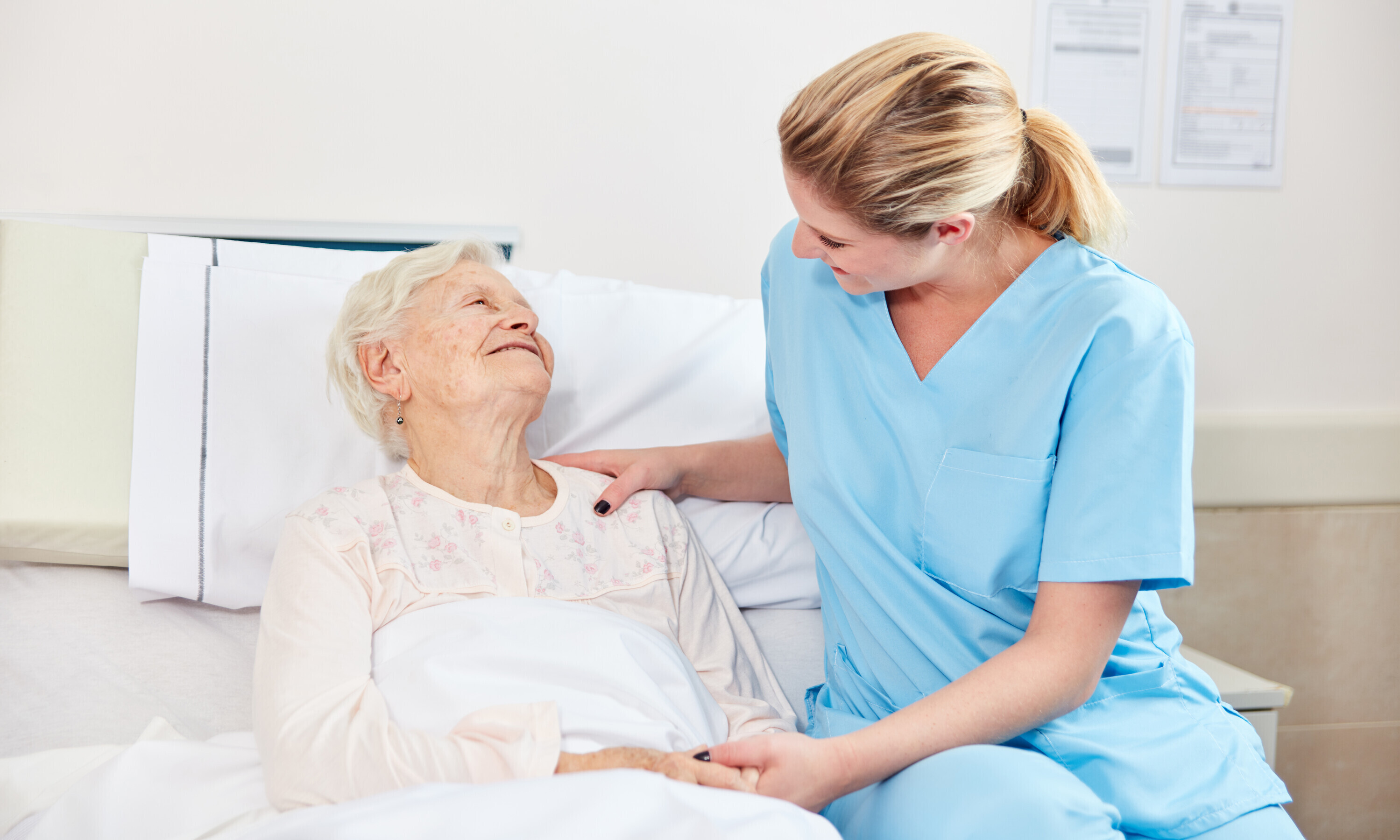 Eine bettlägrige alte Dame wird von einer jungen Pflegerin behandelt.