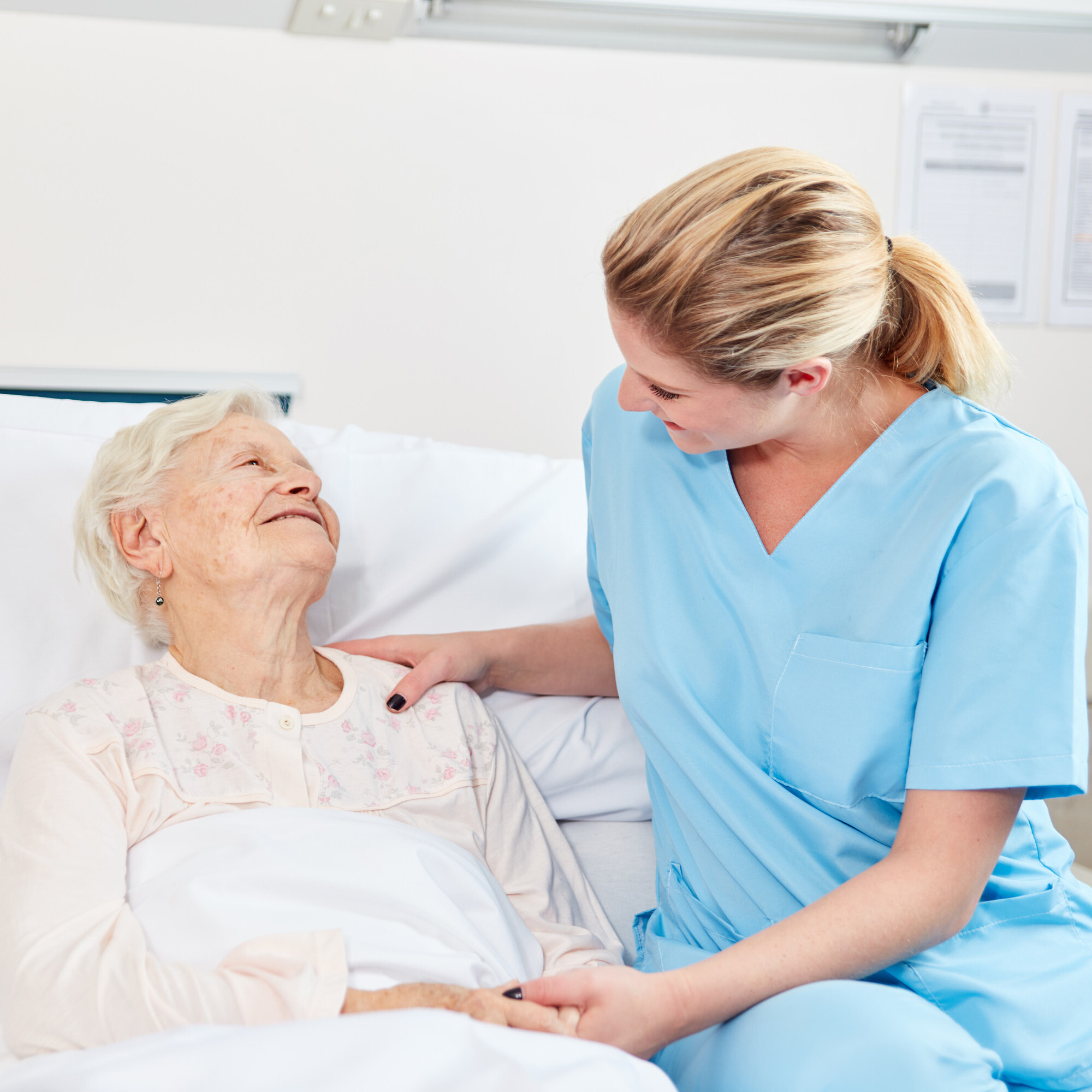 Eine bettlägrige alte Dame wird von einer jungen Pflegerin behandelt.
