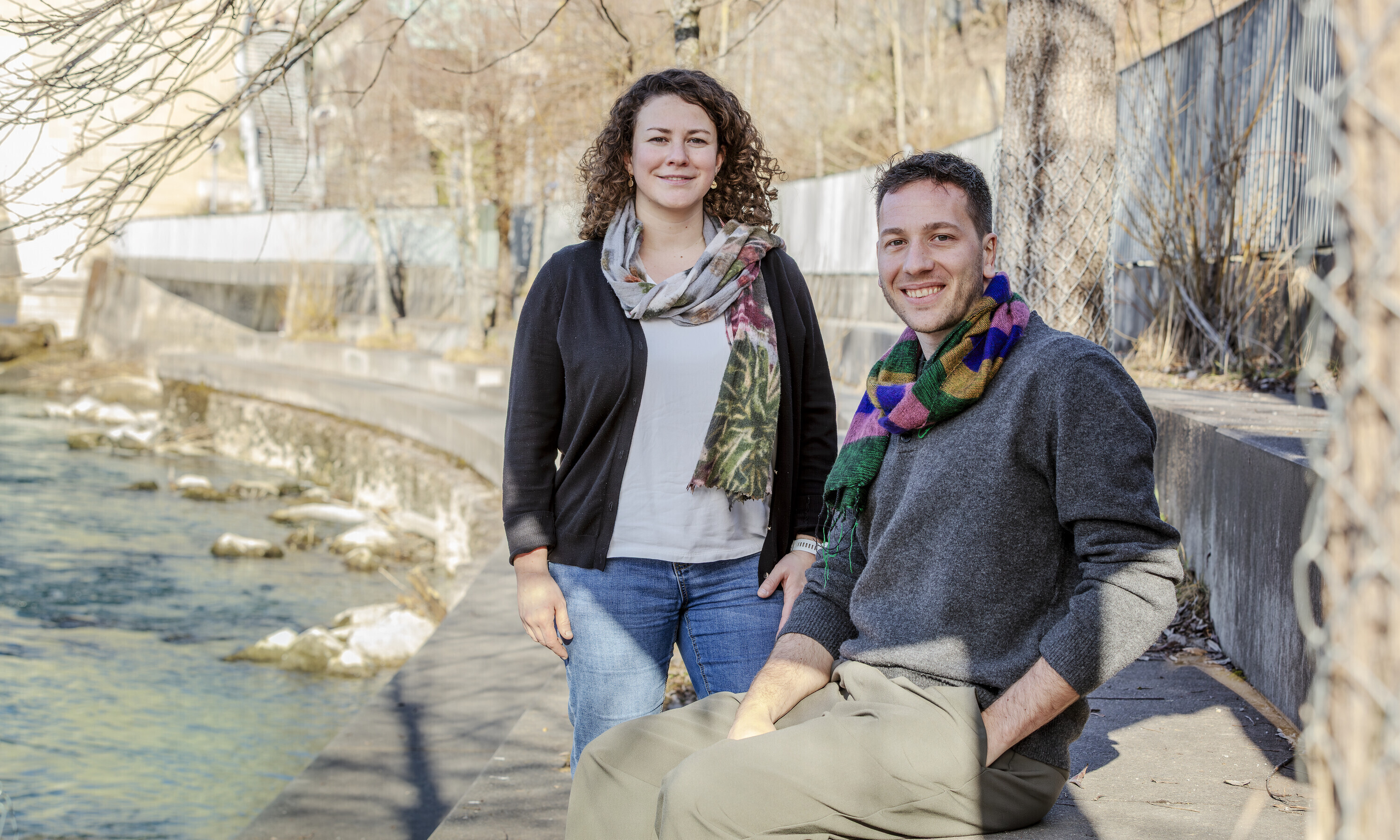 Das Bild zeigt Tamara Kast stehend und Marco Lehmann sitzend auf einer lang gezogenen Steinbank in einer Flusskurve.