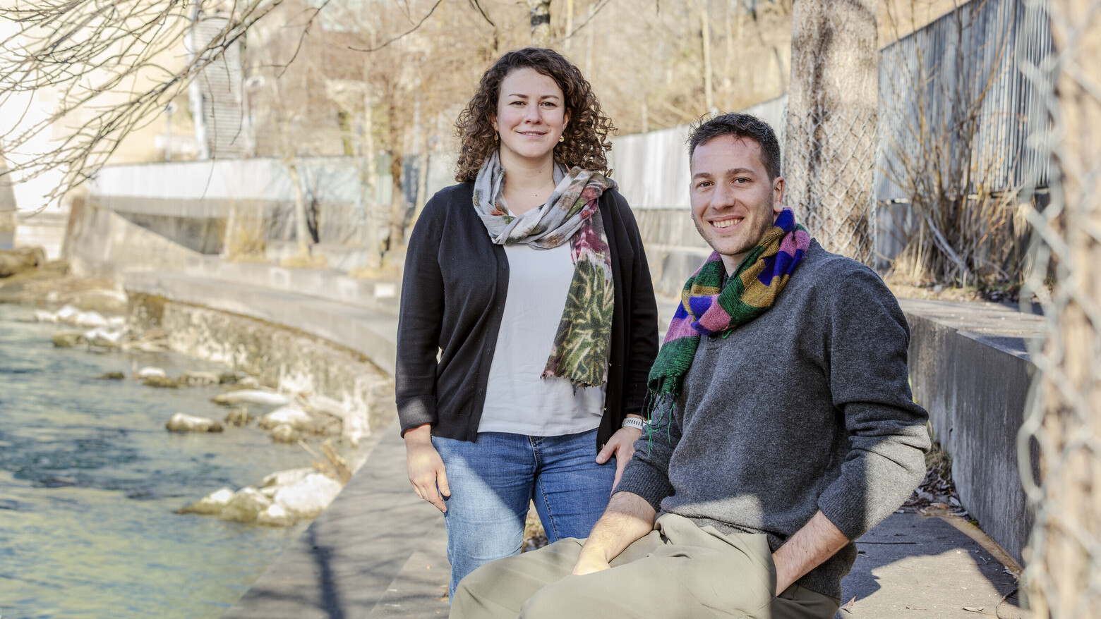Das Bild zeigt Tamara Kast stehend und Marco Lehmann sitzend auf einer lang gezogenen Steinbank in einer Flusskurve.