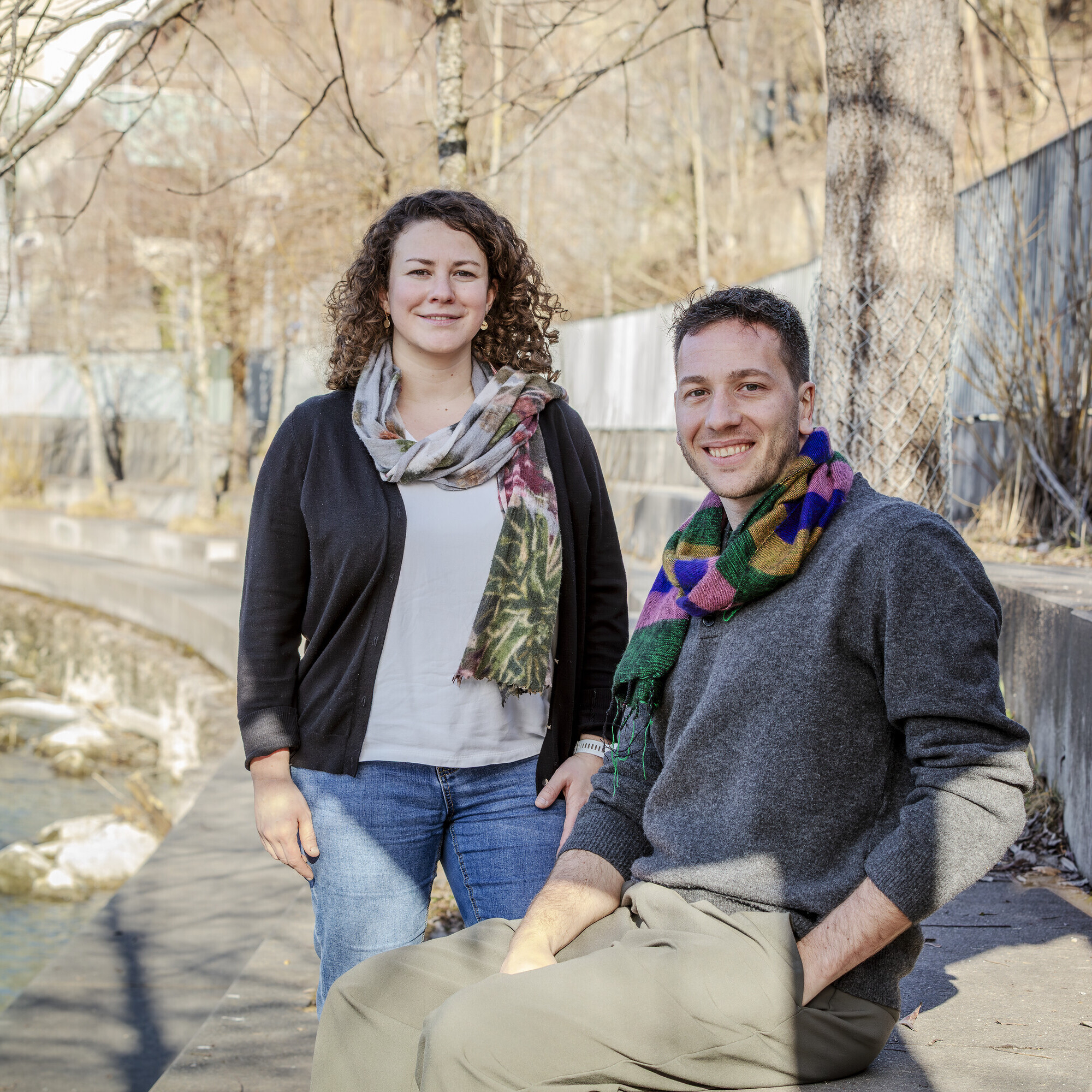 Das Bild zeigt Tamara Kast stehend und Marco Lehmann sitzend auf einer lang gezogenen Steinbank in einer Flusskurve.