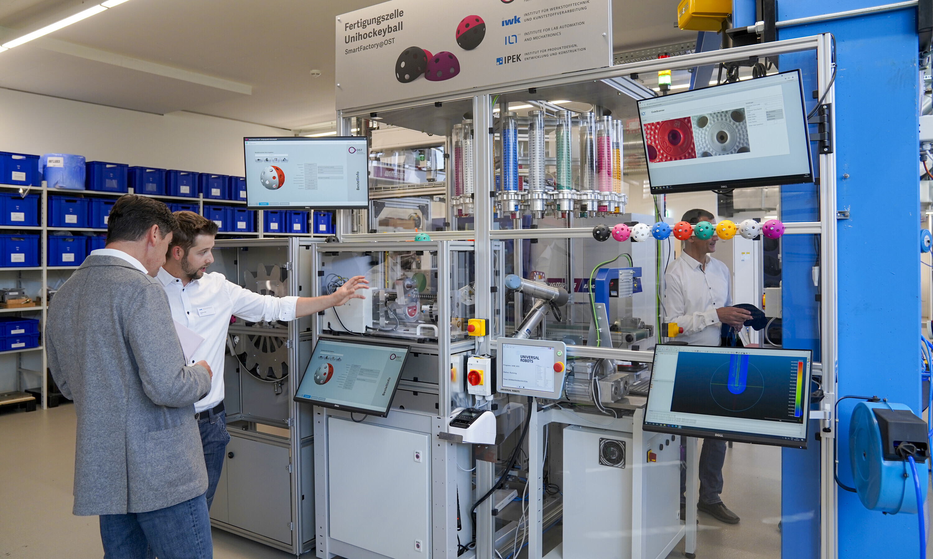 Ein Angestellter aus dem Labor erklärt einem Besucher die Fertigungszelle für Unihockeybälle. 