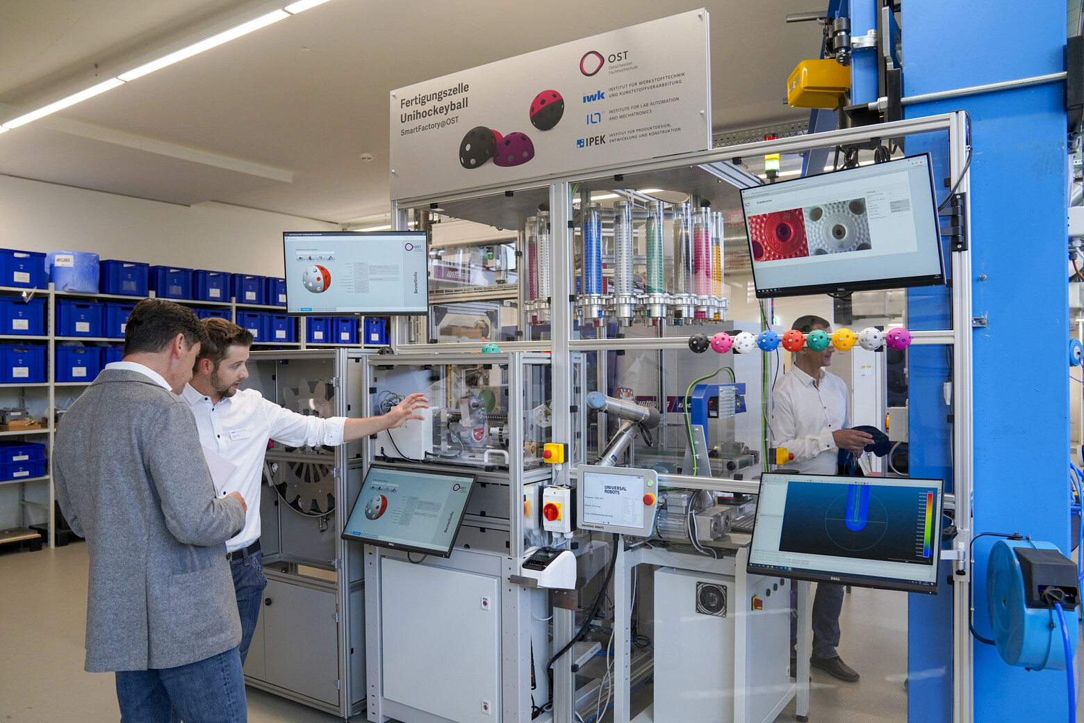 Ein Angestellter aus dem Labor erklärt einem Besucher die Fertigungszelle für Unihockeybälle. 