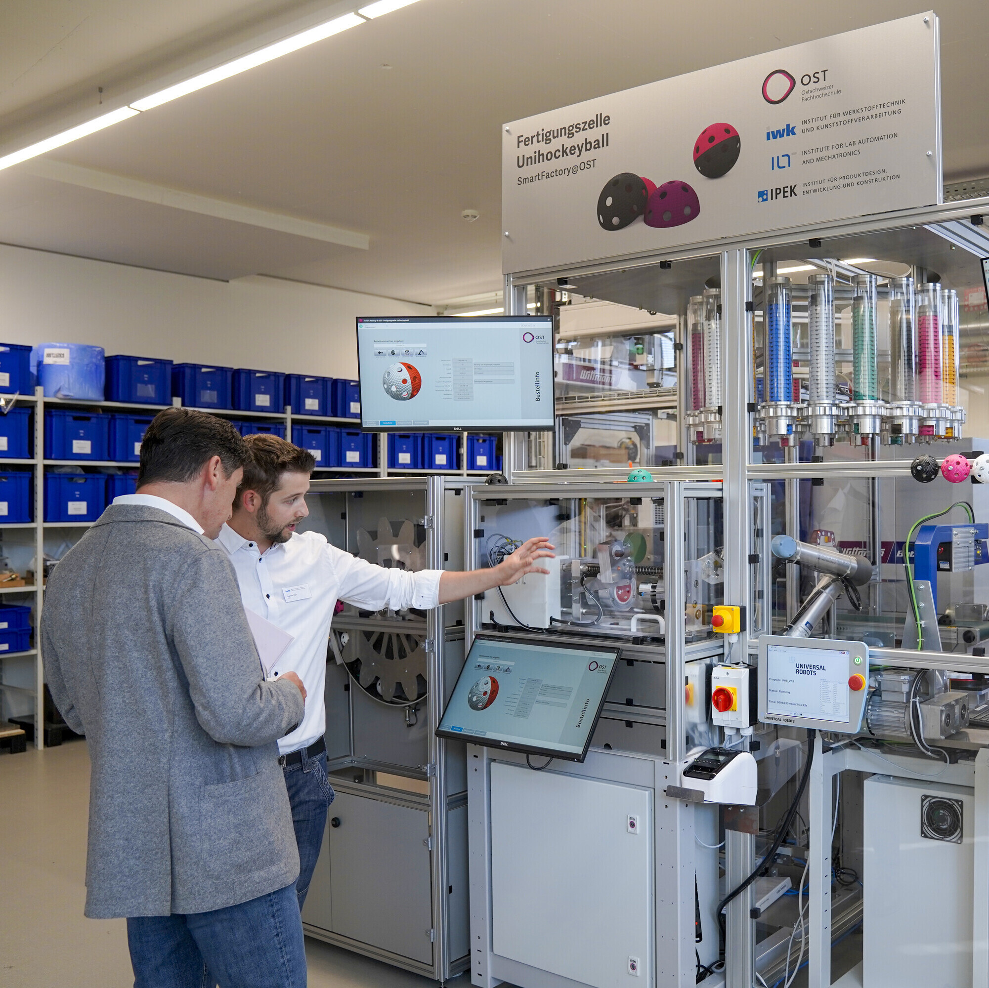 Ein Angestellter aus dem Labor erklärt einem Besucher die Fertigungszelle für Unihockeybälle. 