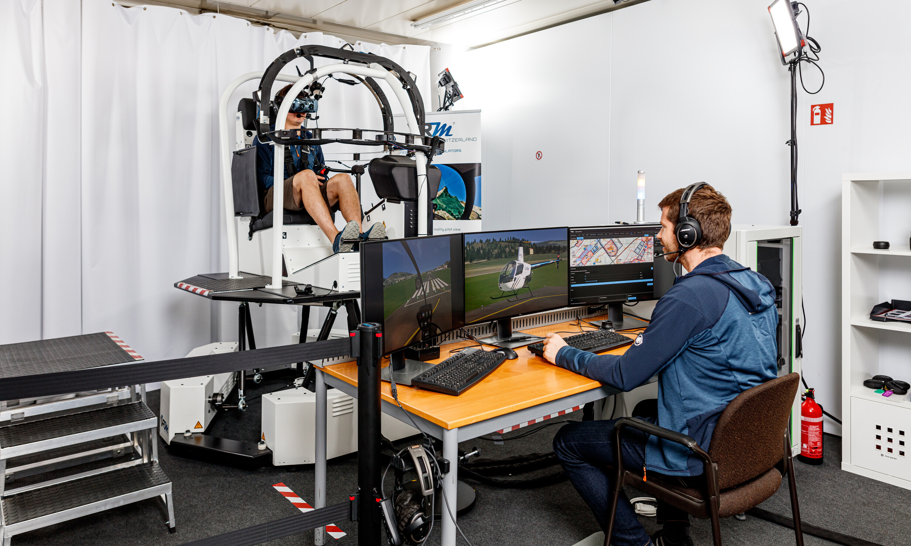 Ein Flugsimulator der VRMotion AG wird auf Herz und Nieren geprüft: Ein Mann sitzt im Simulator, ein weiterer vor mehreren Bildschirmen.