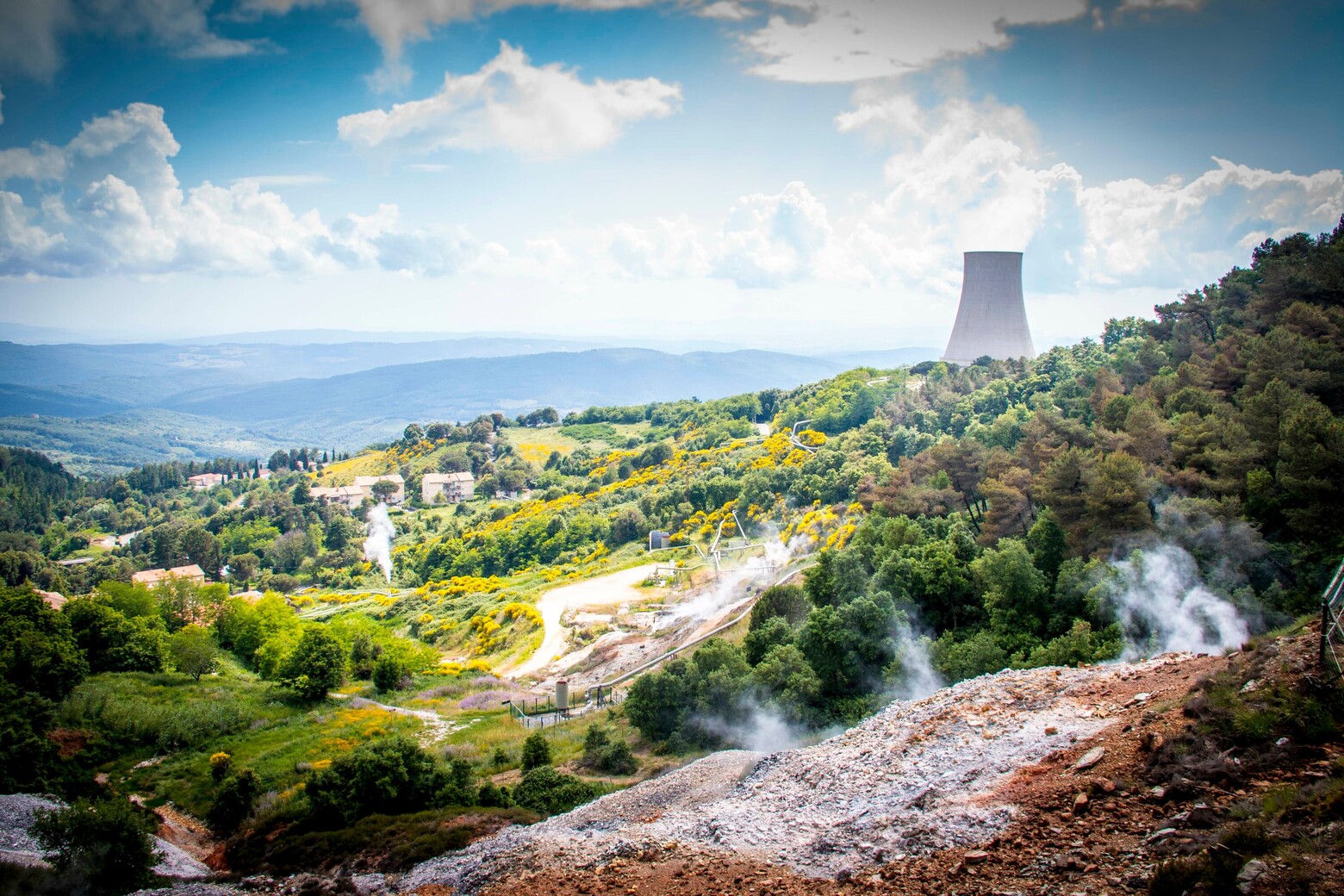 Auf dem Bild sieht man eine Landschaft zwischen Wald und Steinbruch, und im Hintergrund einen Kühlturm eines Atomkraftwerks.