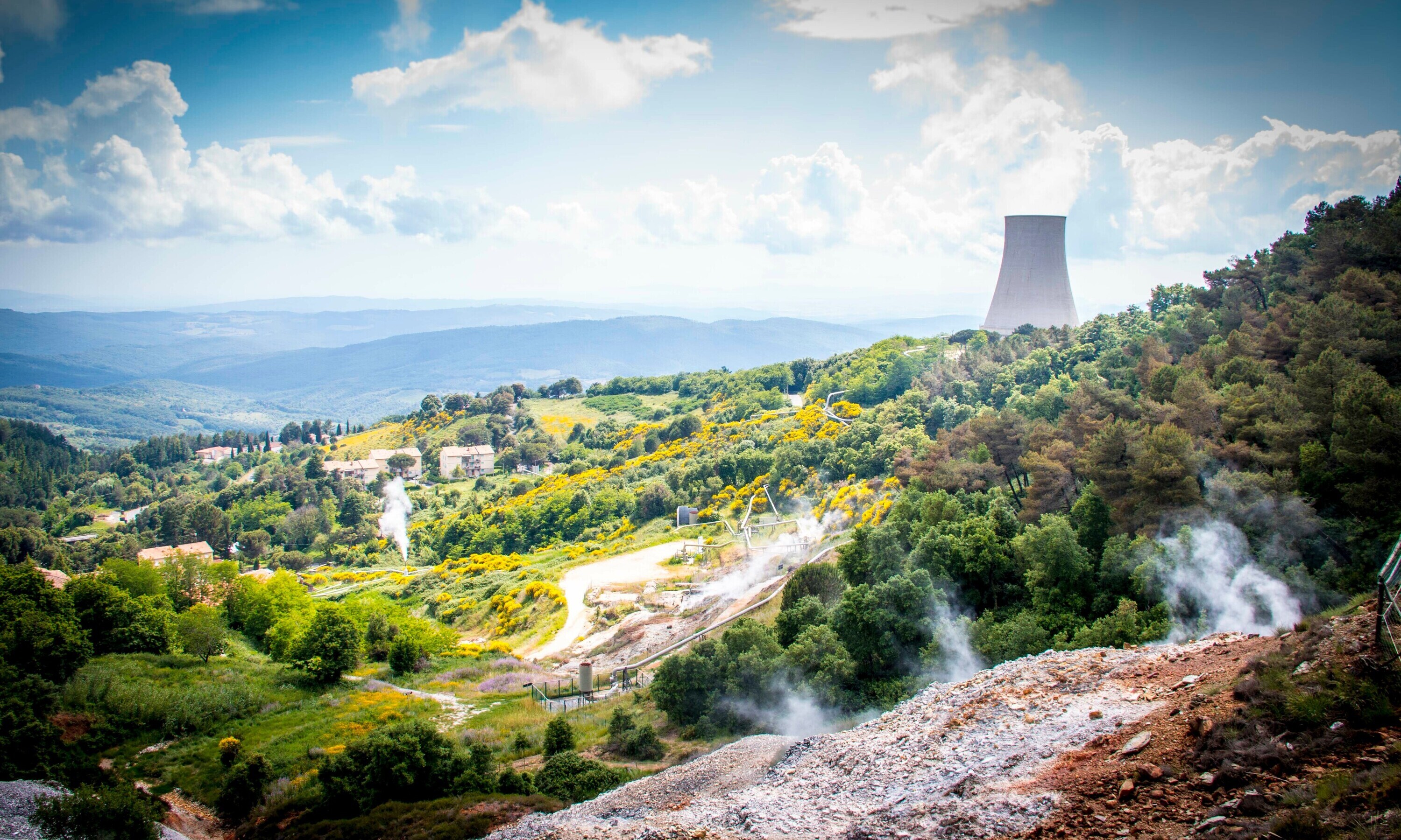 Auf dem Bild sieht man eine Landschaft zwischen Wald und Steinbruch, und im Hintergrund einen Kühlturm eines Atomkraftwerks.