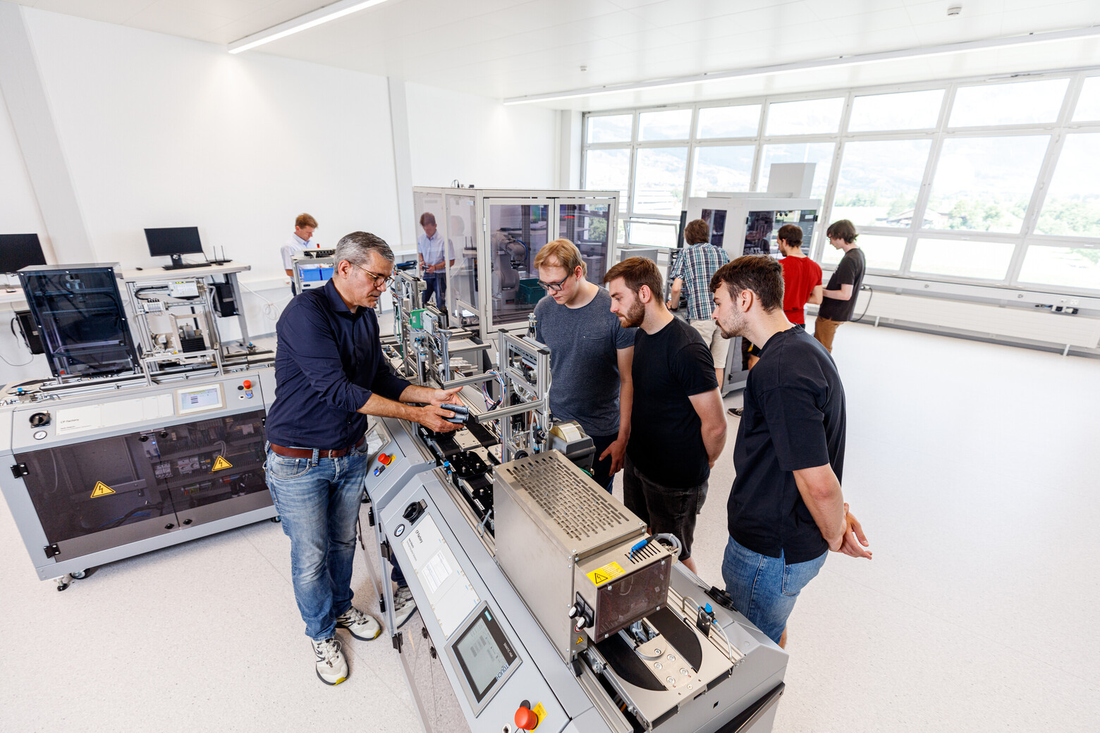 Ein Dozent erklärt drei Studenten einen Prozess in der Hybriden Lernfabrik in Buchs.
