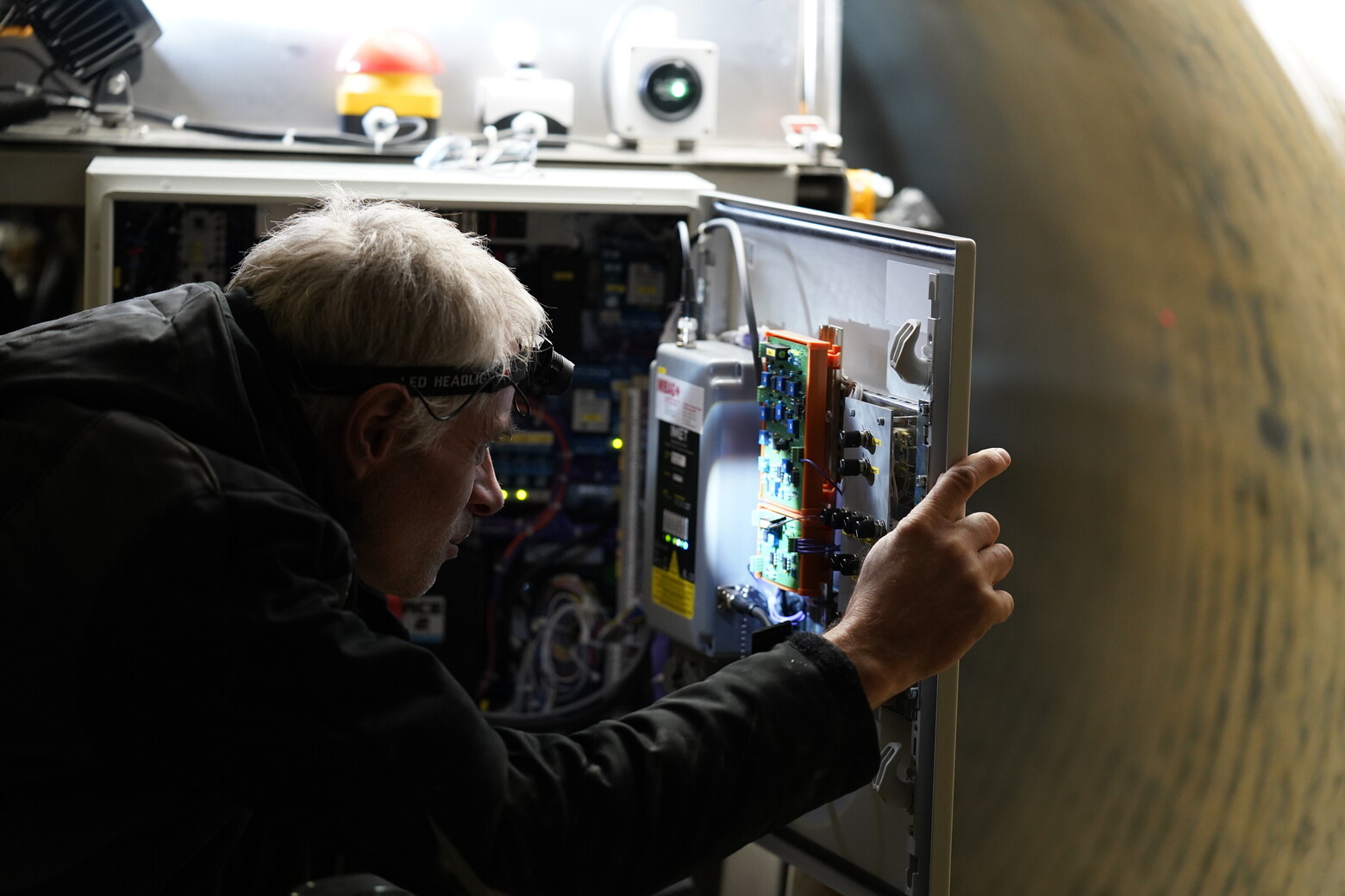 Ein Mann mit Stirnlampe leuchtet in den Schaltkasten der hoch technisierten Spezialmaschine.