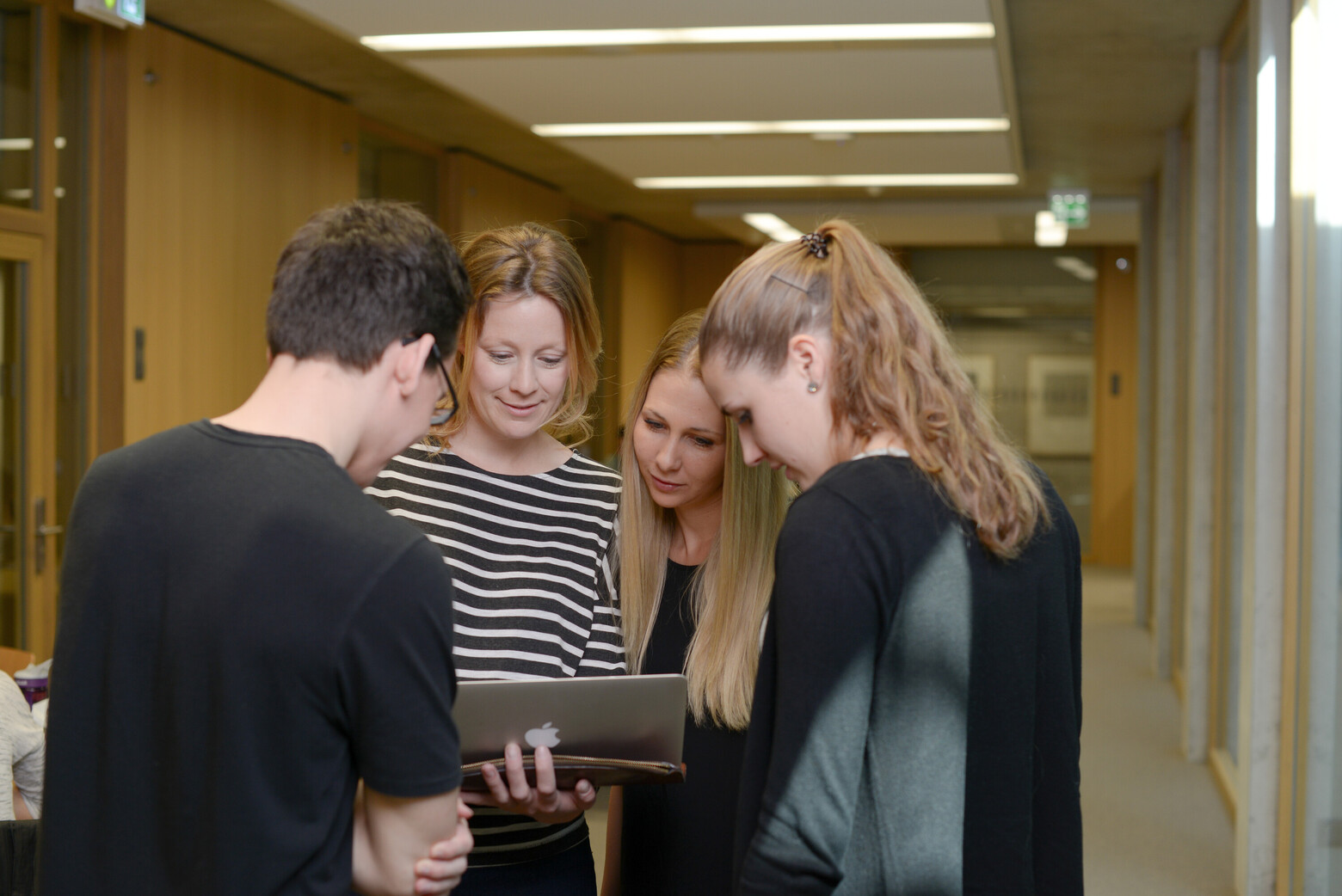 Eine Gruppe von Studierenden beugt sich gemeinsam über einen Laptop.