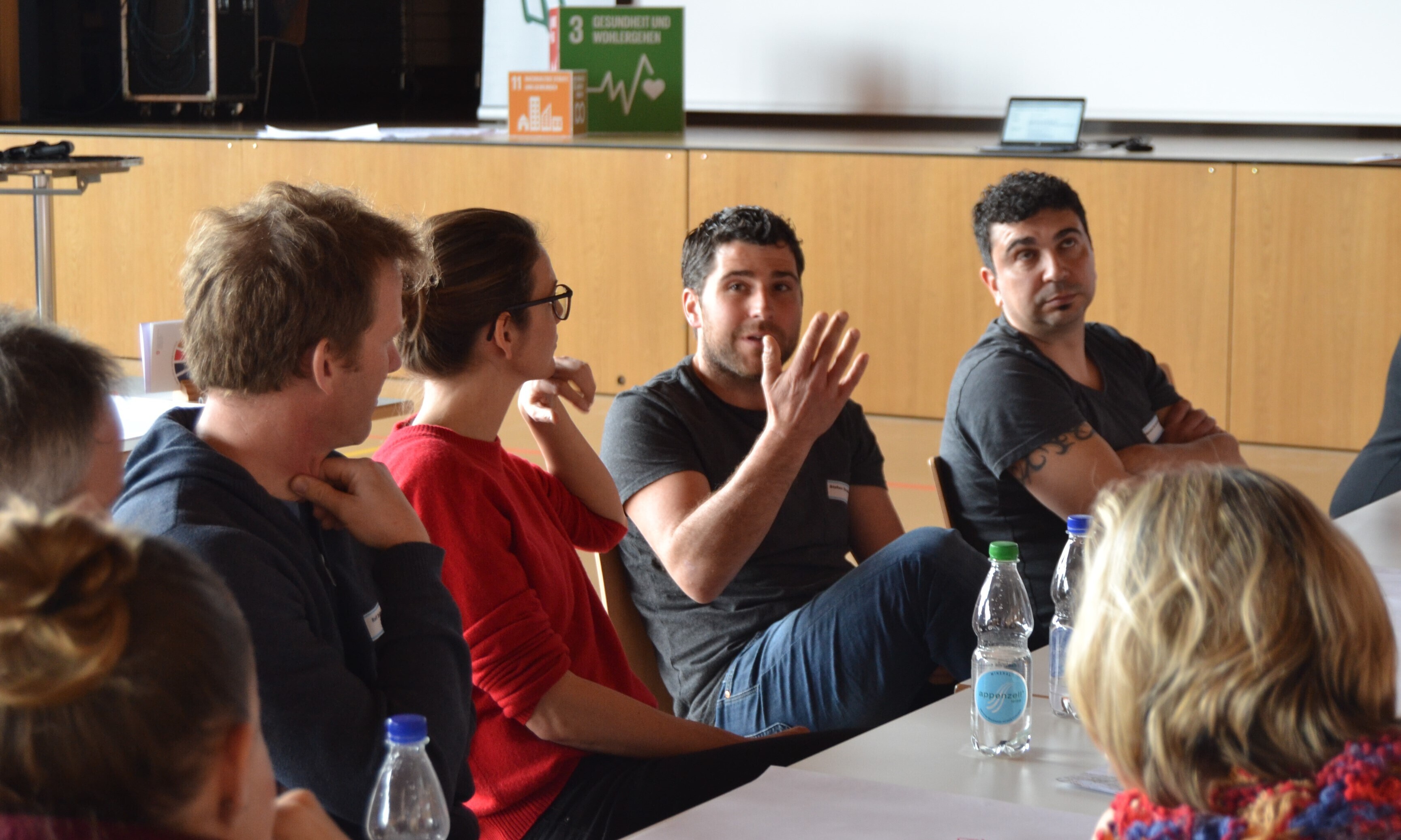 Ein Mann argumentiert mit den Händen, während der Rest des Tisches ihm aufmerksam zuhört. 