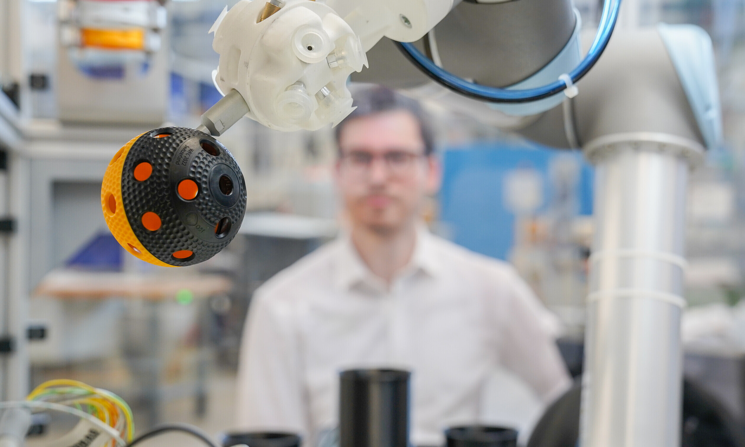 Auf dieser Nahaufnahme ist im Vordergrund ein Unihockeyball in der Maschine zu sehen, dahinter der Forscher mit Schutzbrille.