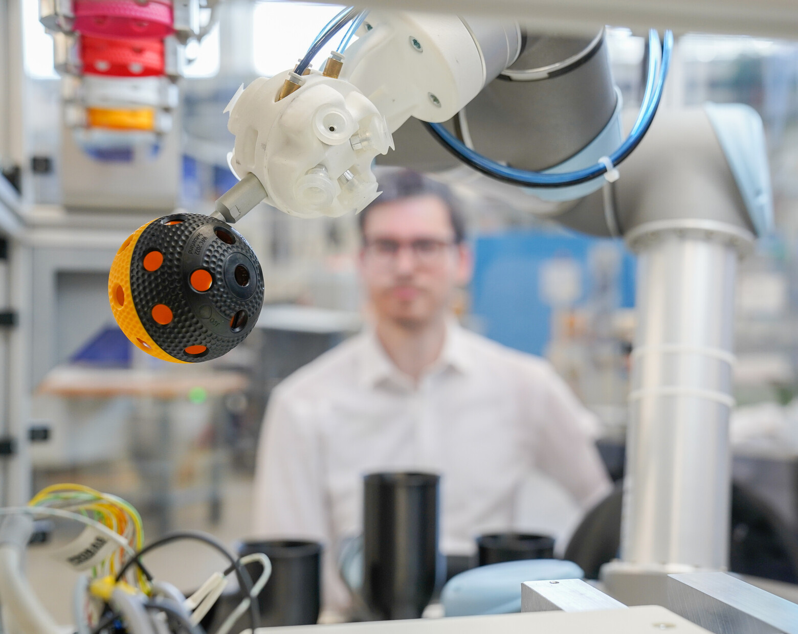 Auf dieser Nahaufnahme ist im Vordergrund ein Unihockeyball in der Maschine zu sehen, dahinter der Forscher mit Schutzbrille.