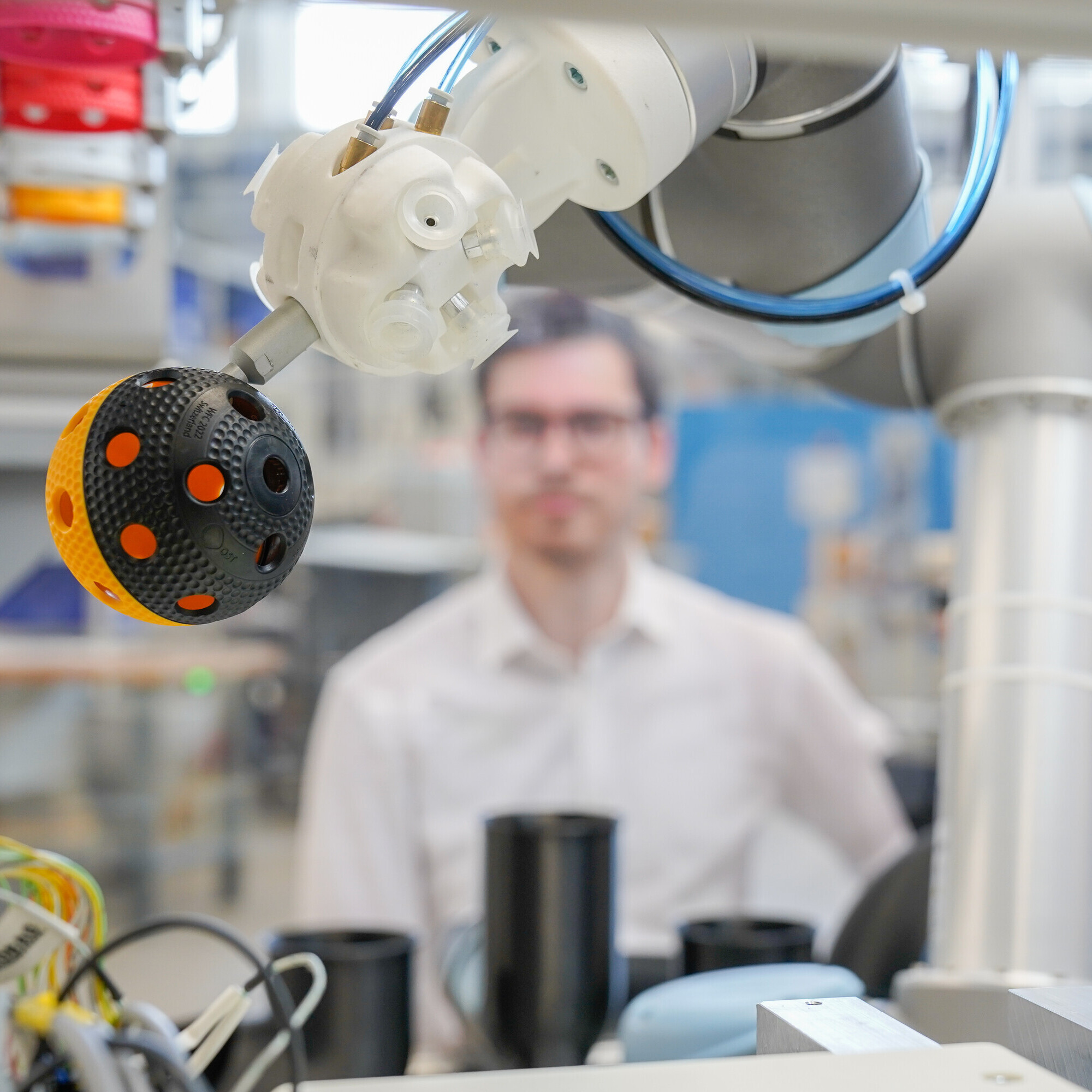 Auf dieser Nahaufnahme ist im Vordergrund ein Unihockeyball in der Maschine zu sehen, dahinter der Forscher mit Schutzbrille.