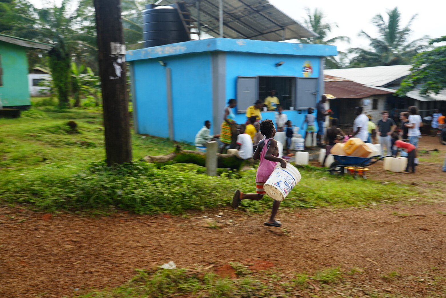 Mit Kübeln ausgerüstet holen Kinder und Erwachsene beim blauen Wasserkiosk sauberes Trinkwasser für ihre Familien.