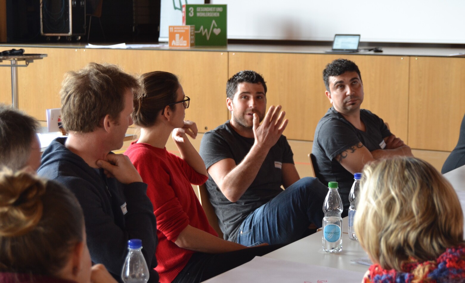 Ein Mann argumentiert mit den Händen, während der Rest des Tisches ihm aufmerksam zuhört. 