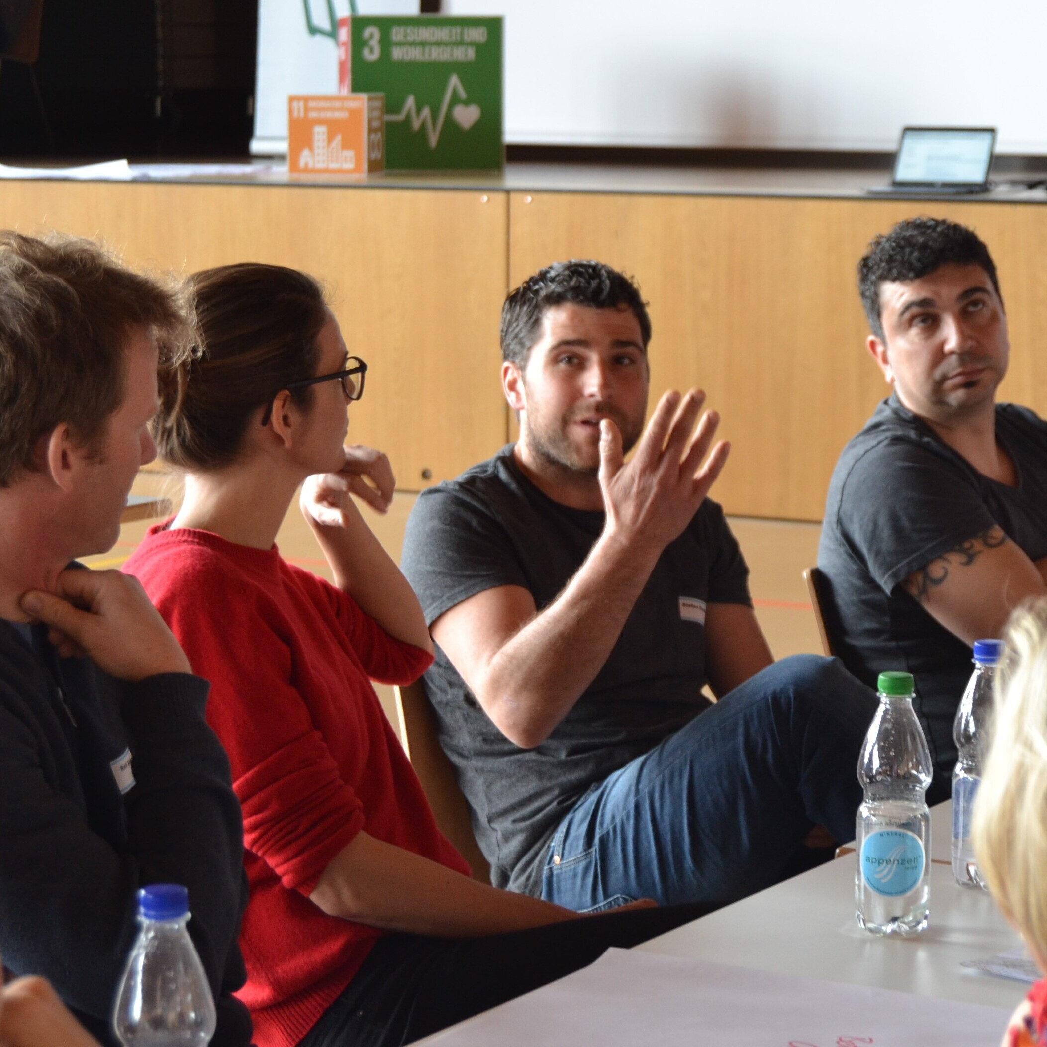 Ein Mann argumentiert mit den Händen, während der Rest des Tisches ihm aufmerksam zuhört. 