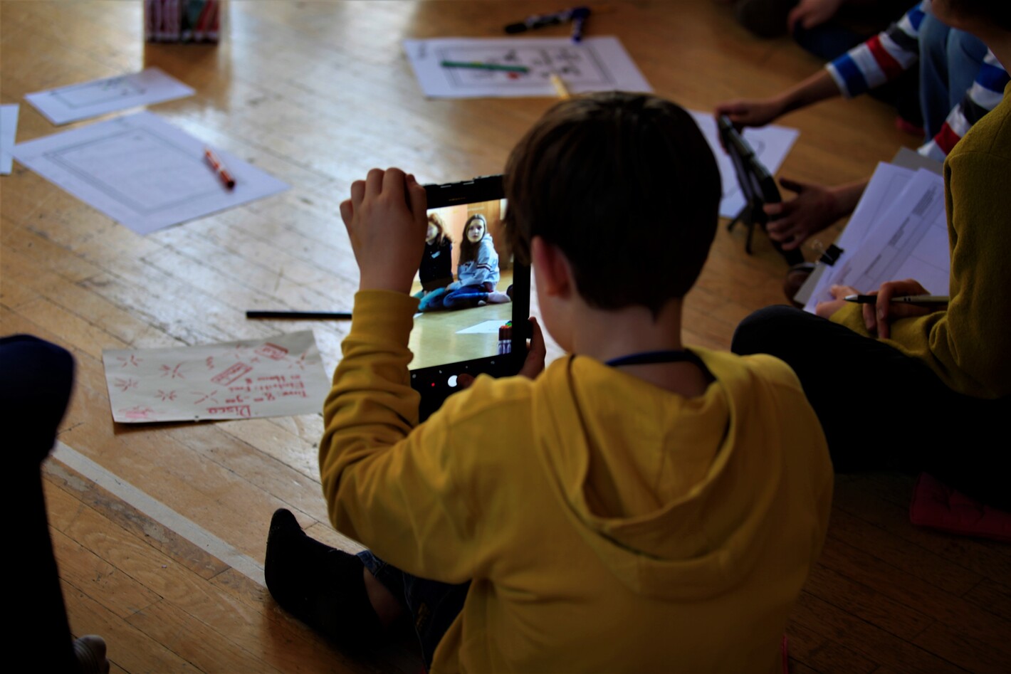 Ein Kind fotografiert mit seinem Tablet andere Kinder.
