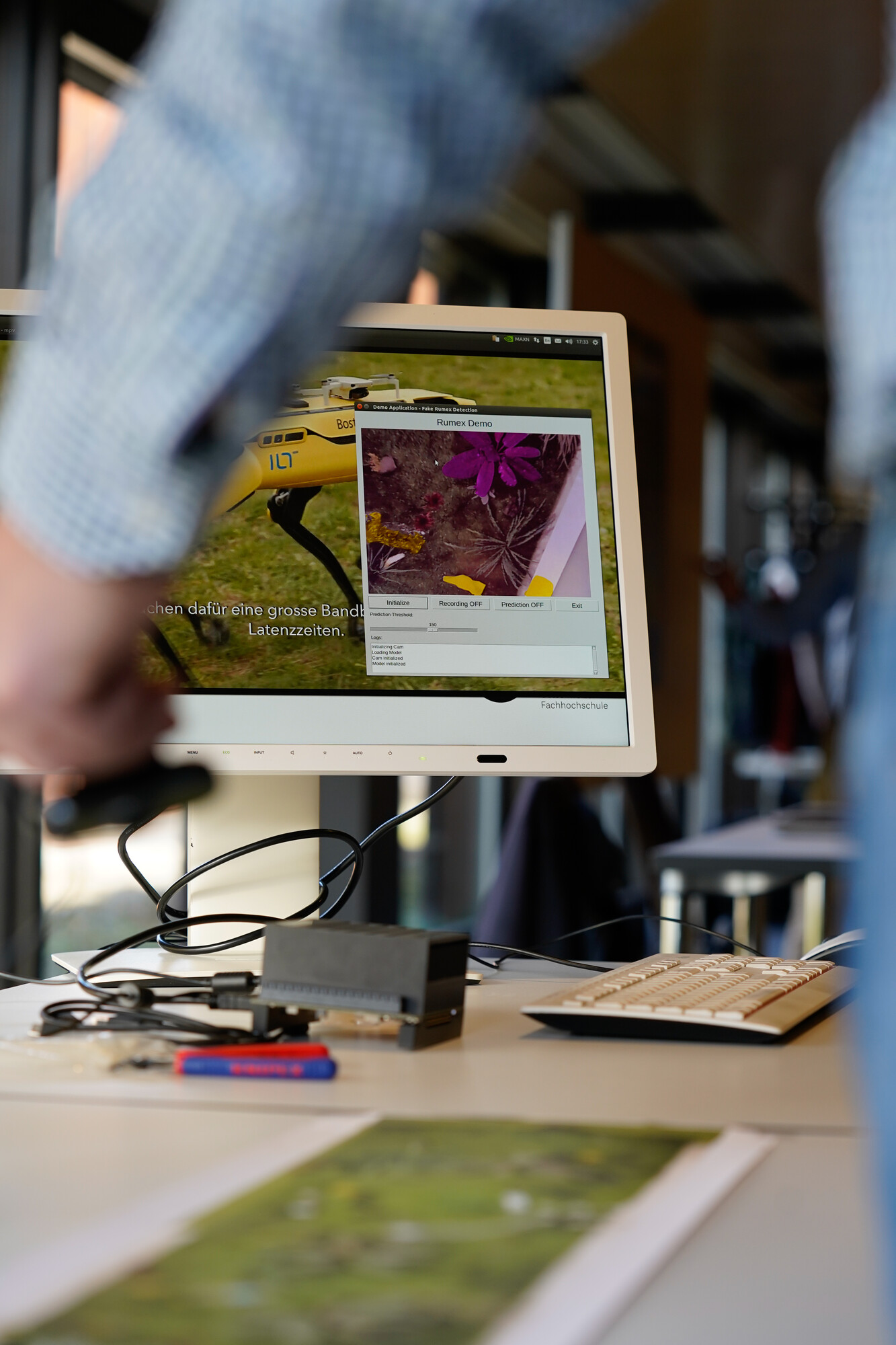 Auf einem flachen Bildschirm ist eine Anwendung zu sehen, bei der eine KI Gegenstände und Pflanzen aus der Luft erkennt.