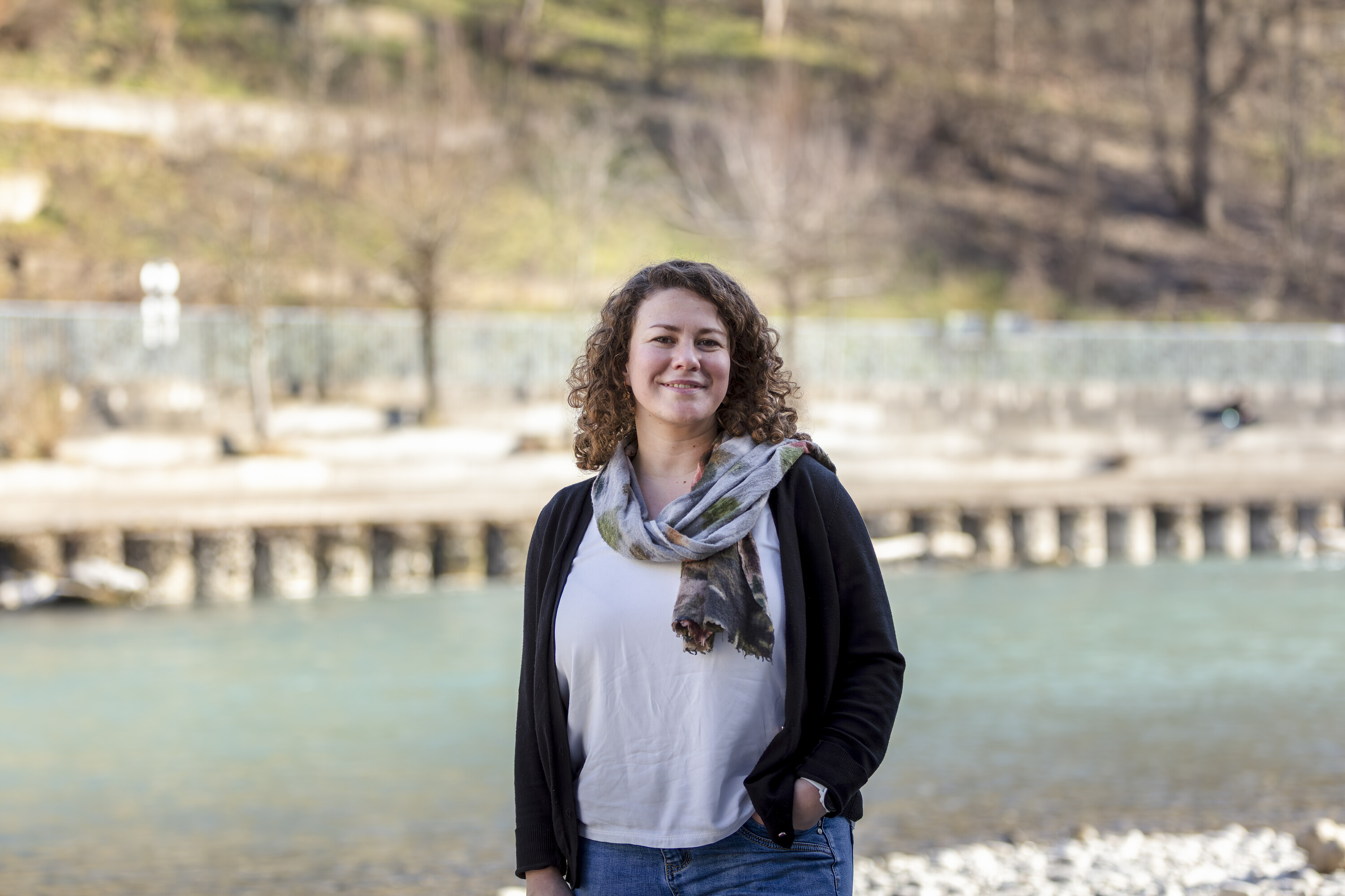  Tamara Kast steht vor einem Fluss in einer kargen Winterlandschaft. Eine Hand steckt locker in ihrer Jeans.
